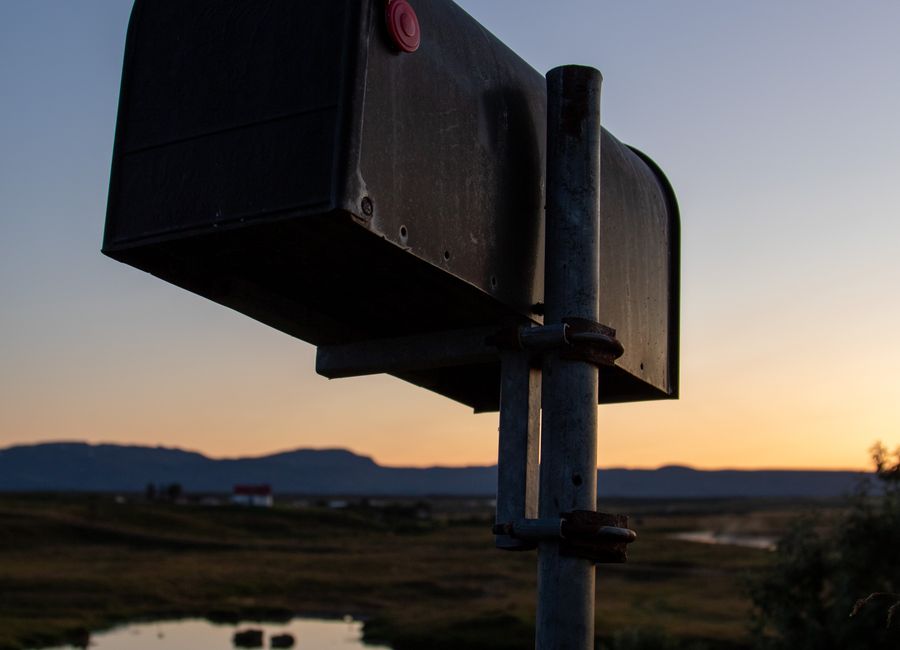 Solitary rural mailbox silhouetted against a sunset over open land